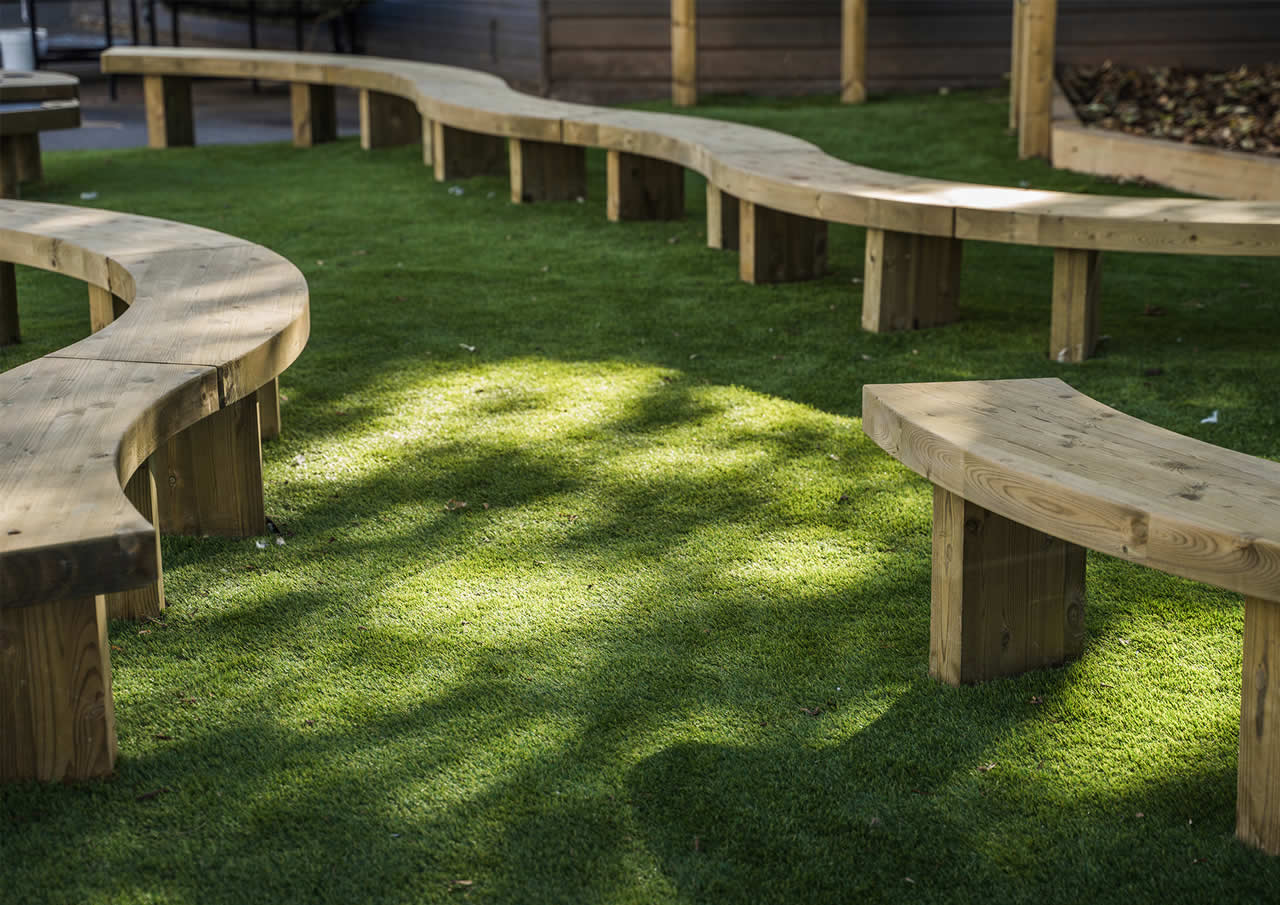 Curvy wooden bench seating installed on artificial grass