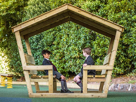 A wooden play pod with two boys sitting down