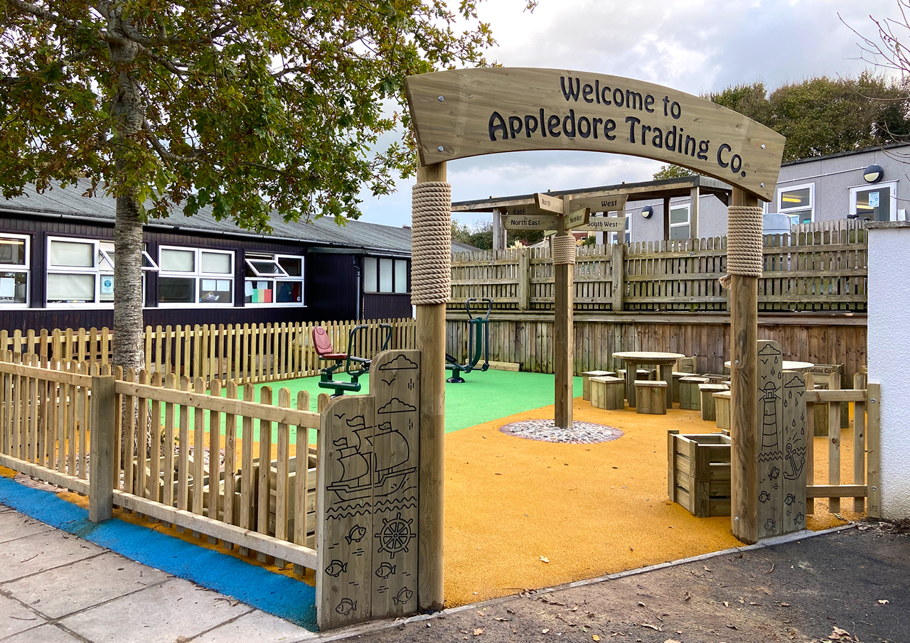 A curved wooden archway at the entrance to a school play ground with colourful safety surfacing