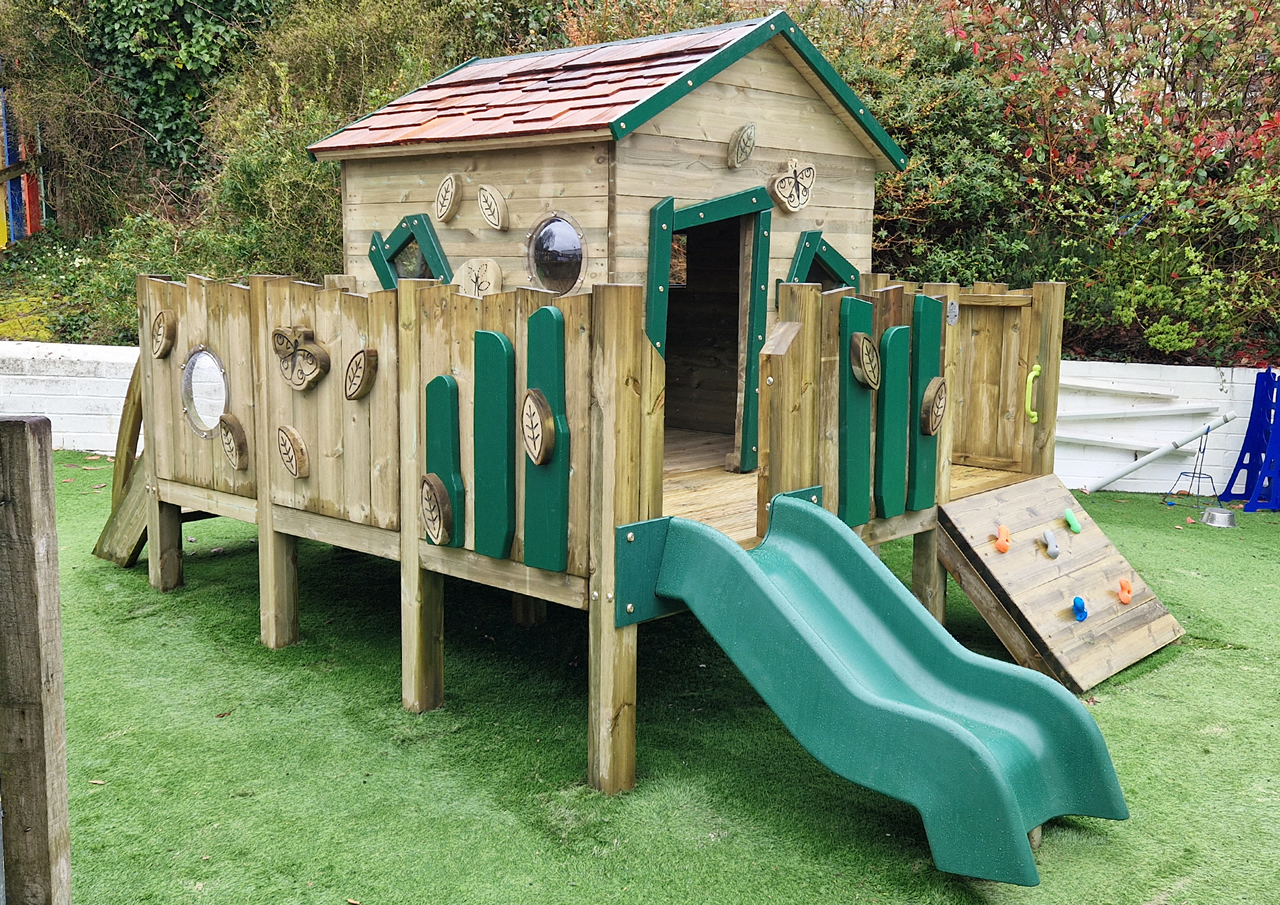 A wooden childrens playhouse with green plastic slide