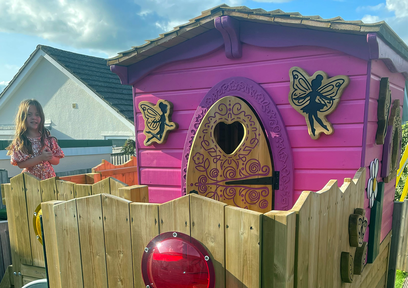 A wooden play house painted in pink adorned with fairies